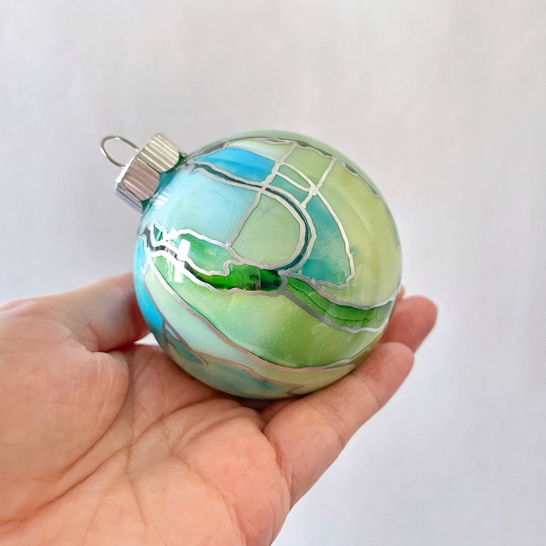 Bring a bright, colorful bauble to the tree. These hand painted ornaments are swirled with shades of aqua blue and green with silver highlights. Created by Sarah John Afana for schemata on Etsy.