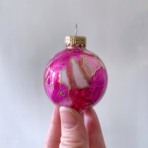 This hand painted glass ornament is swirled with bright, hot pink and rich, deep red with gold highlights. Each ornament is a unique piece and cannot be duplicated. Created by Sarah John Afana for Schemata on Etsy.