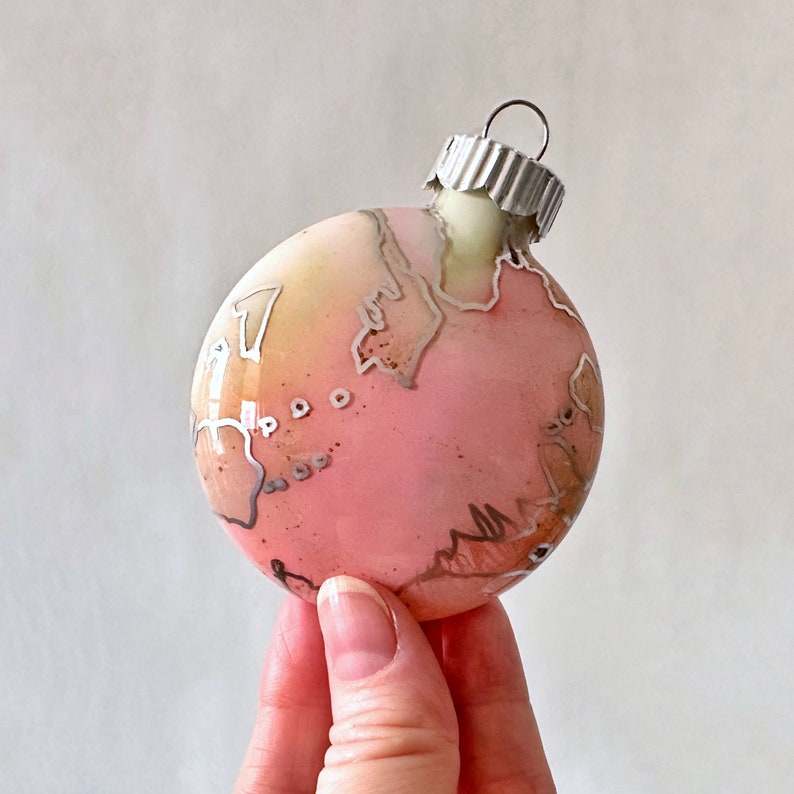 Swirling with cotton candy pink with silver highlights, this one of a kind, hand painted glass ornament will make unique additions to any Christmas tree. Created by Sarah John Afana for schemata on Etsy.