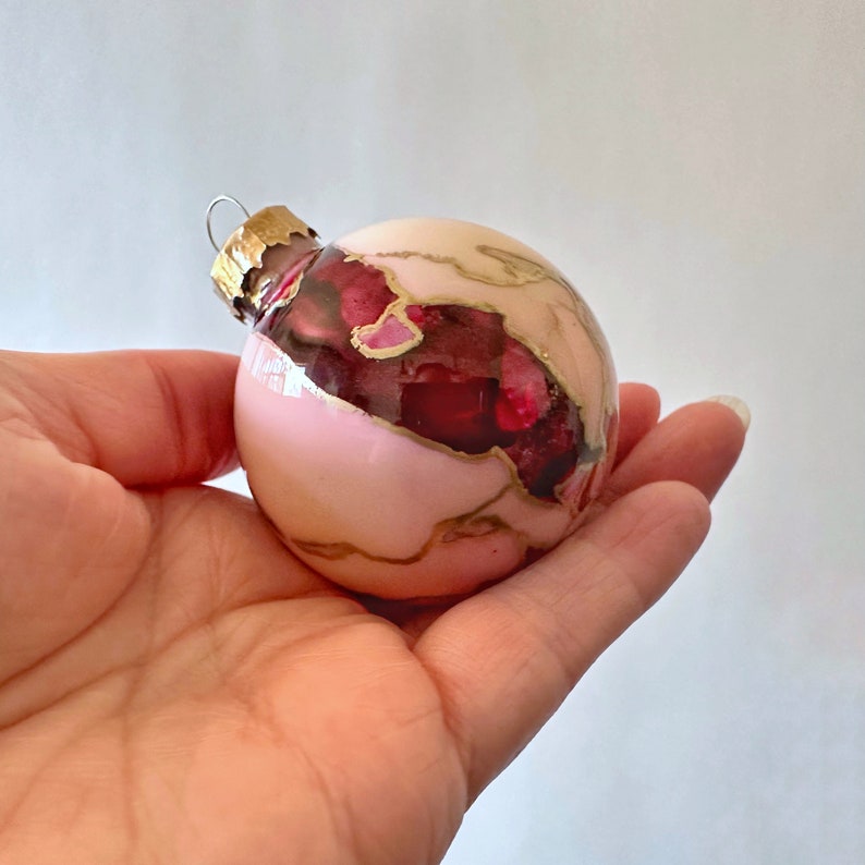 Rich burgundy red swirls with a creamy pink background creating a unique pattern accented with hand-drawn gold highlights in these one-of-a-kind hand-painted Christmas ornaments. Created by Sarah John Afana for schemata on Etsy.