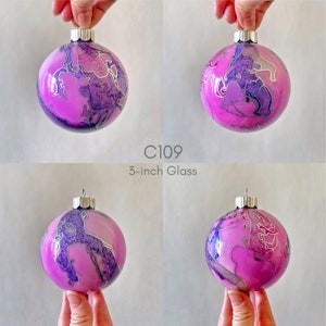 May include: A 3-inch glass Christmas ornament with a pink and purple marbled design and silver accents. C109.