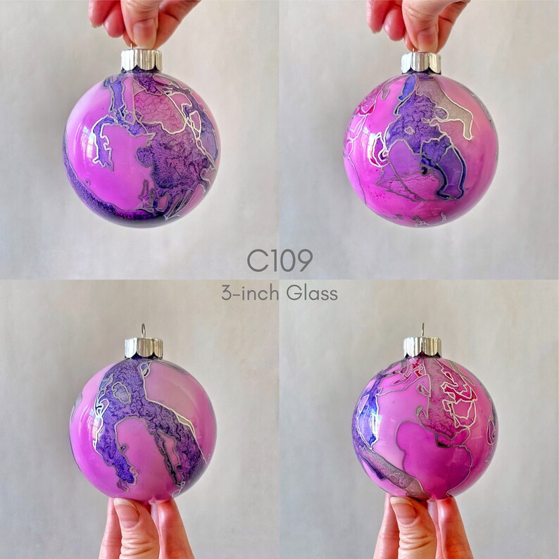 May include: A 3-inch glass Christmas ornament with a pink and purple marbled design and silver accents. C109.
