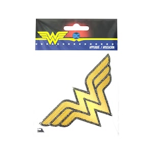 May include: Gold Wonder Woman logo iron-on patch with a black outline. The patch is packaged on a white card with the DC Comics logo and the text "Applique / Aplicacion".