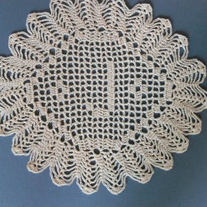 May include: A beige crocheted doily with a delicate, intricate pattern. The doily is circular and has a scalloped edge.