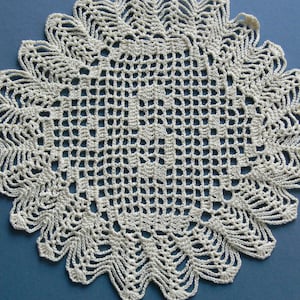 May include: A white crocheted doily with a delicate, intricate design. The doily has a circular shape with a scalloped edge.