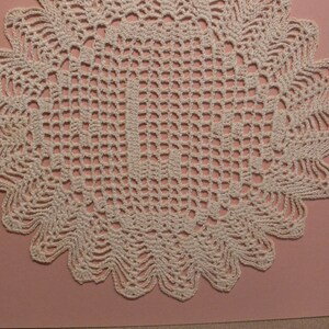 May include: A white crocheted doily with a delicate, intricate design. The doily has a circular shape with a scalloped edge.