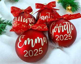 Adorno navideño personalizado con forma de bola, nombre en vinilo dorado y lazo rojo.
