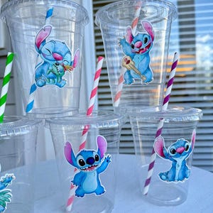 May include: Six clear plastic cups with blue and white cartoon character stickers of Stitch from Lilo & Stitch. The cups have red and white striped straws.