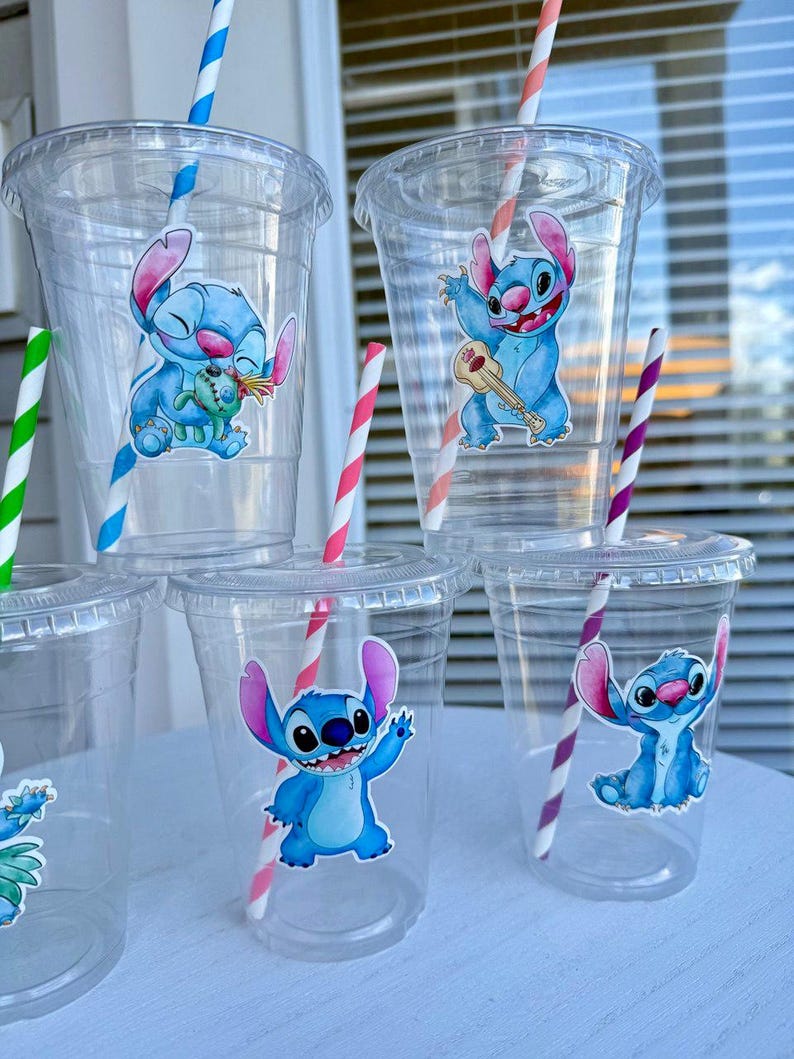 May include: Six clear plastic cups with blue and white cartoon character stickers of Stitch from Lilo & Stitch. The cups have red and white striped straws.