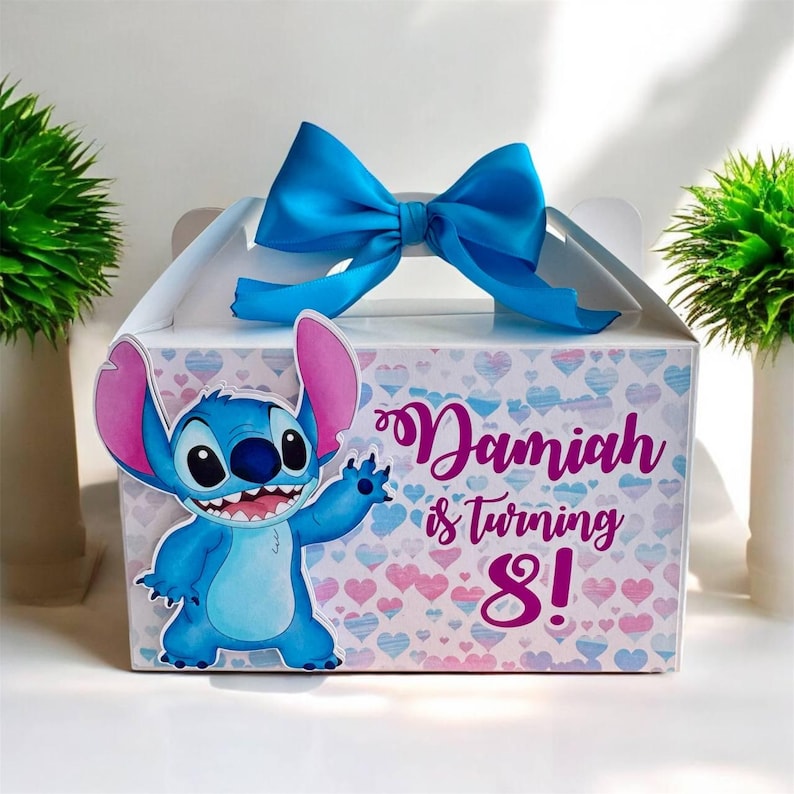 May include: A blue and pink party favor box with a blue bow. The box features a cartoon Stitch character and the text "Damiah is turning 8!"