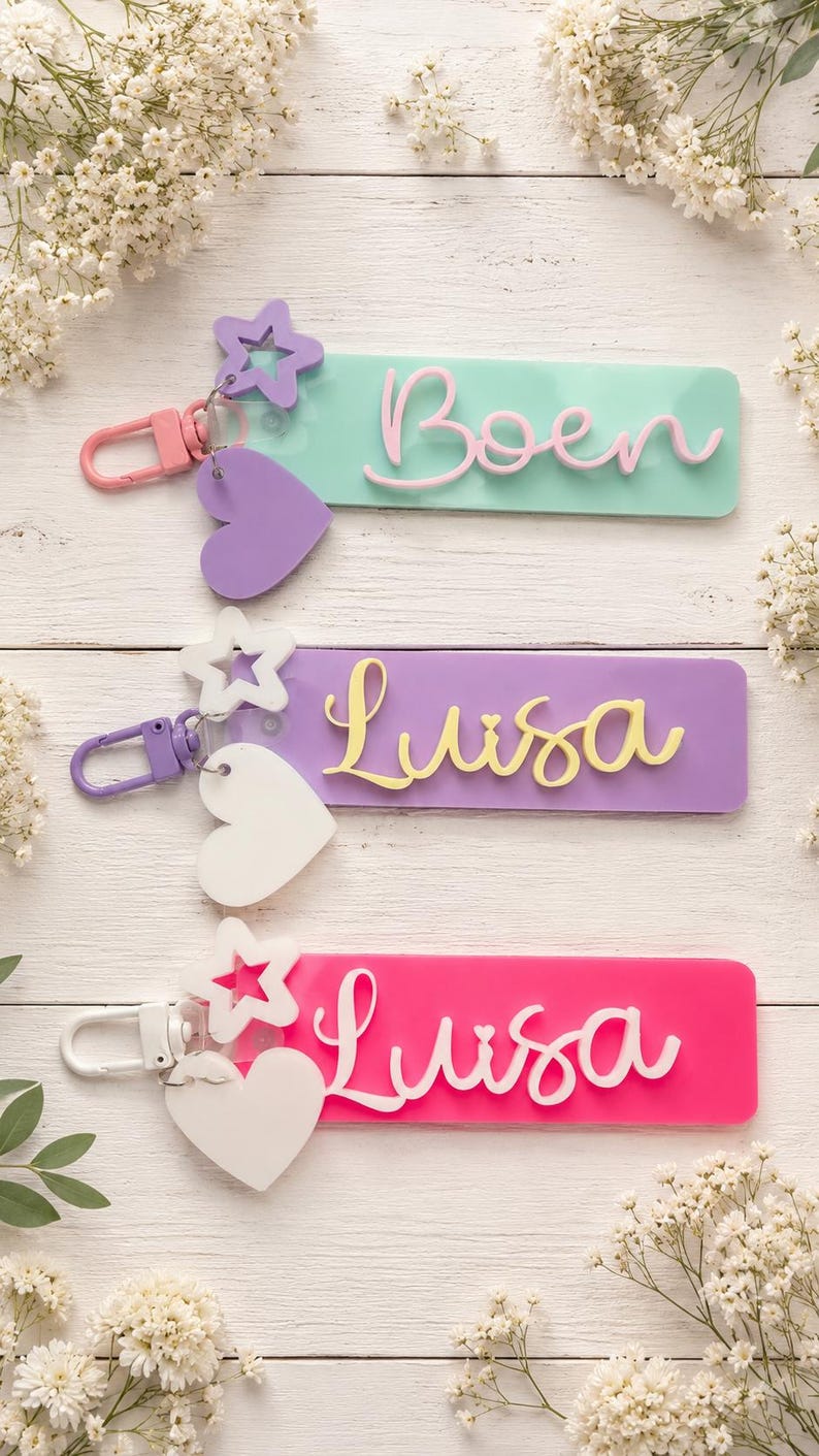 Puede incluir: Tres llaveros rectangulares de acr&iacute;lico con dijes de estrella y coraz&oacute;n. El llavero superior es verde menta con el nombre Boen en rosa. El del medio es morado con el nombre Luisa en amarillo. El inferior es rosa intenso con el nombre Luisa en blanco.
