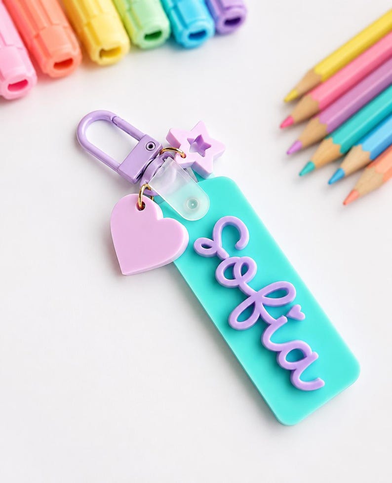 Puede incluir: Un llavero rectangular de acr&iacute;lico turquesa con el nombre Sofia en letras cursivas moradas en relieve. El llavero incluye un cierre de mosquet&oacute;n morado, un peque&ntilde;o dije de estrella morada y un dije de coraz&oacute;n morado claro.