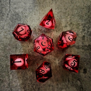 May include: A set of seven translucent red polyhedral dice for tabletop gaming. Each die features a glowing white core and black ink numbering. The central twenty-sided die displays a crescent moon symbol in place of the number twenty.