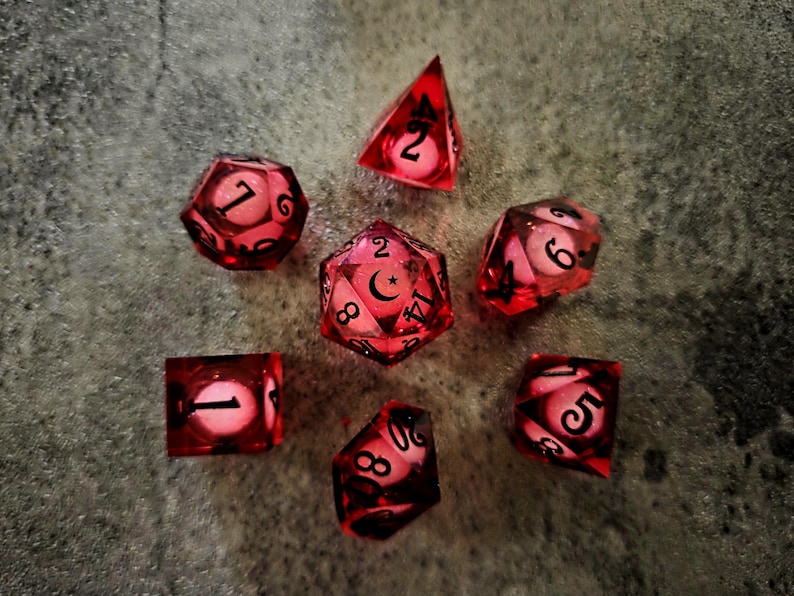 May include: A set of seven translucent red polyhedral dice for tabletop gaming. Each die features a glowing white core and black ink numbering. The central twenty-sided die displays a crescent moon symbol in place of the number twenty.