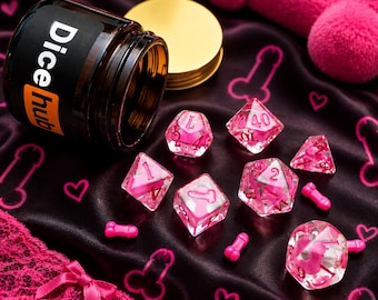 Peut inclure: Un ensemble de dés polyédriques roses translucides avec des formes phalliques internes et des chiffres roses, accompagné d'un pot en verre ambré étiqueté Dice hub avec un couvercle doré, sur un tissu noir à motifs phalliques et cœurs roses.