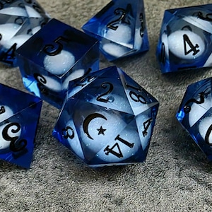 May include: A collection of blue and white dice with black numbering. The dice are made of a translucent material, with a white core and blue edges. The dice are of various shapes, including six-sided and multi-sided dice.