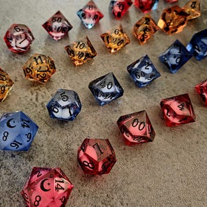 May include: A collection of translucent polyhedral dice in various colours including red, blue, and amber. Each die features black numbers and some include moon and star symbols. The set includes various shapes such as d20, d12, d10, d8, d6, and d4, arranged in a scattered pattern across the frame.