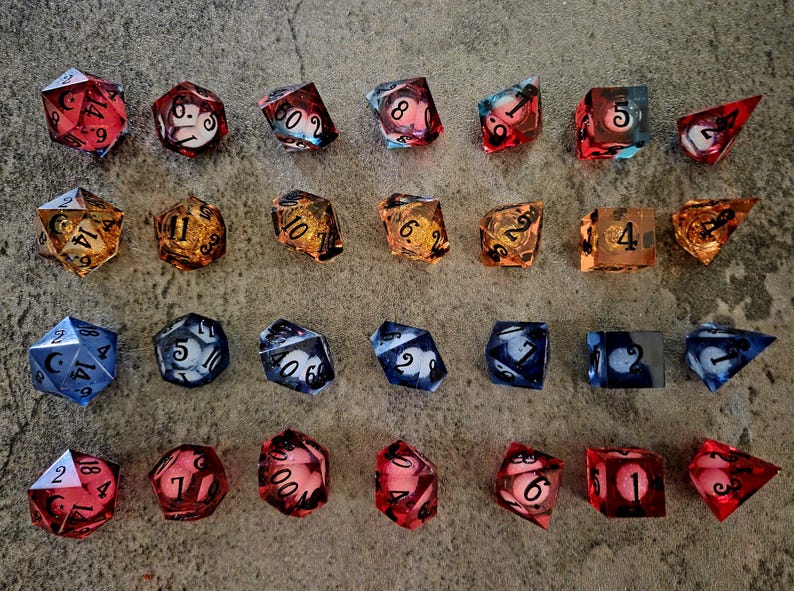 May include: A collection of twenty-eight polyhedral dice arranged in four rows of seven. The dice feature various translucent colours including red, orange, and blue, with internal spherical shapes and black numerical markings on their surfaces.