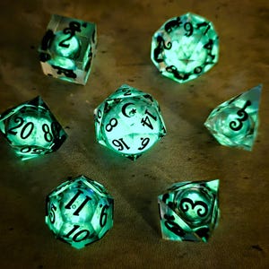 Puede incluir: Conjunto de siete dados verdes brillantes para juegos de mesa. Cada dado tiene números negros y una forma geométrica única. Los dados se iluminan desde dentro, creando un efecto visual llamativo.
