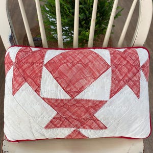 May include: A rectangular throw pillow featuring a quilted white and red fabric pattern. The design consists of geometric shapes in a red textured fabric set against a white background, finished with a solid red fabric border around the edges.