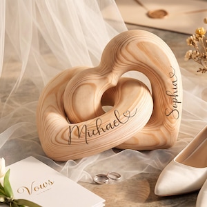 May include: Two interlocking light-colored wooden heart sculptures with visible wood grain. The left heart is engraved with the name Michael and a small heart icon, while the right heart is engraved with the name Sophia and a small heart icon.