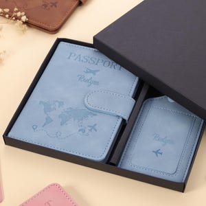 May include: A light blue passport holder and luggage tag set presented in a black gift box. The passport holder is embossed with a world map and the name "Raelynn". The luggage tag also features the name "Raelynn" and an aeroplane icon.