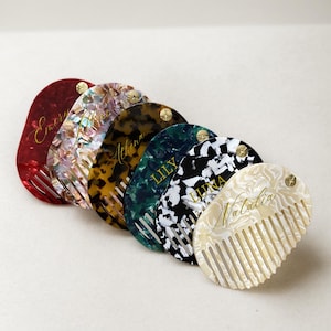 Può includere: Una collezione di pettini personalizzati in vari colori e motivi. I pettini sono nelle tonalità di rosso, iridescente, tartarugato, verde, bianco e nero e crema. Ogni pettine ha un nome in oro.