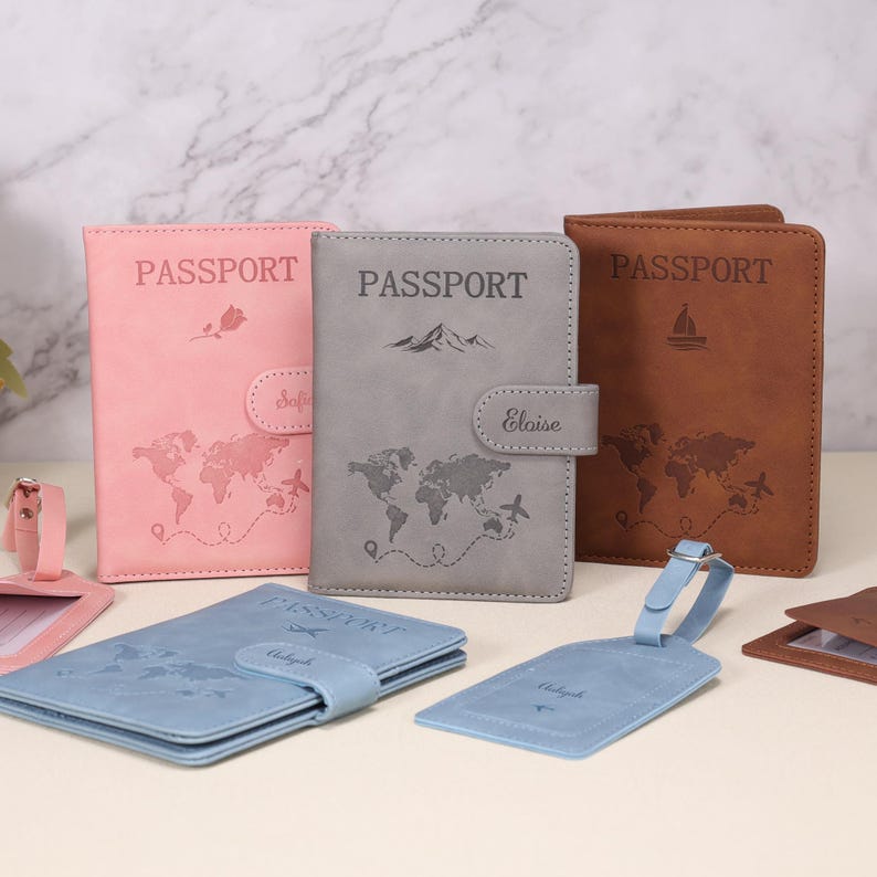 Op de afbeelding: Een verzameling paspoorthouders en bagagelabels in verschillende kleuren. De paspoorthouders zijn roze, grijs en bruin, elk met een wereldkaart en het woord "PASSPORT" in reli&euml;f. De bagagelabels zijn blauw. Elk item heeft een uniek ontwerp.