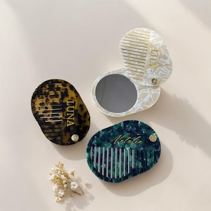 Op de afbeelding: Drie gepersonaliseerde compacte spiegels met kammen. E&eacute;n heeft een luipaardprint met "LUNA" in gouden letters. Een andere is wit met een marmerpatroon en "LILY". De derde is groen met "Natalia".