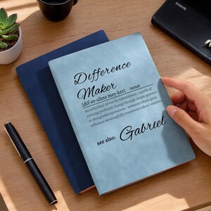 Könnte beinhalten: Ein blaues und hellblaues Notizbuch mit dem Text "Difference Maker" und einer Definition des Wortes. Der Name "Gabriel" steht unter der Definition.