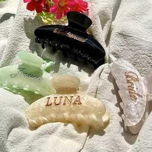 以下が含まれることがあります： 黒、ライトグリーン、クリーム、白の大理石調のヘアクリップ4点。黒いクリップにはゴールドでBridesmaid、ライトグリーンにはJessica、クリームにはLUNA、白の大理石調にはBrideという文字がそれぞれ刻まれています。