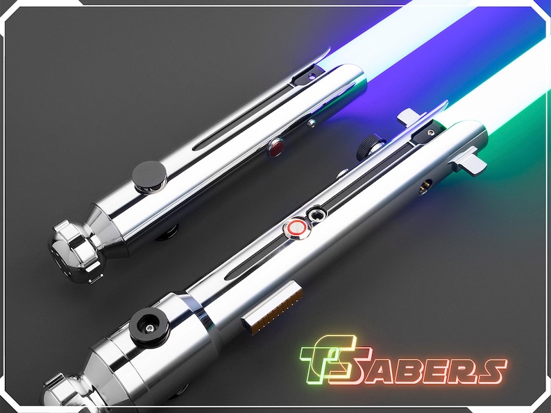 Puede incluir: Dos sables de luz plateados con hojas iluminadas en azul, verde y blanco. Los mangos tienen detalles en negro y rojo. El logotipo "TSabers" se muestra en verde ne&oacute;n y naranja.