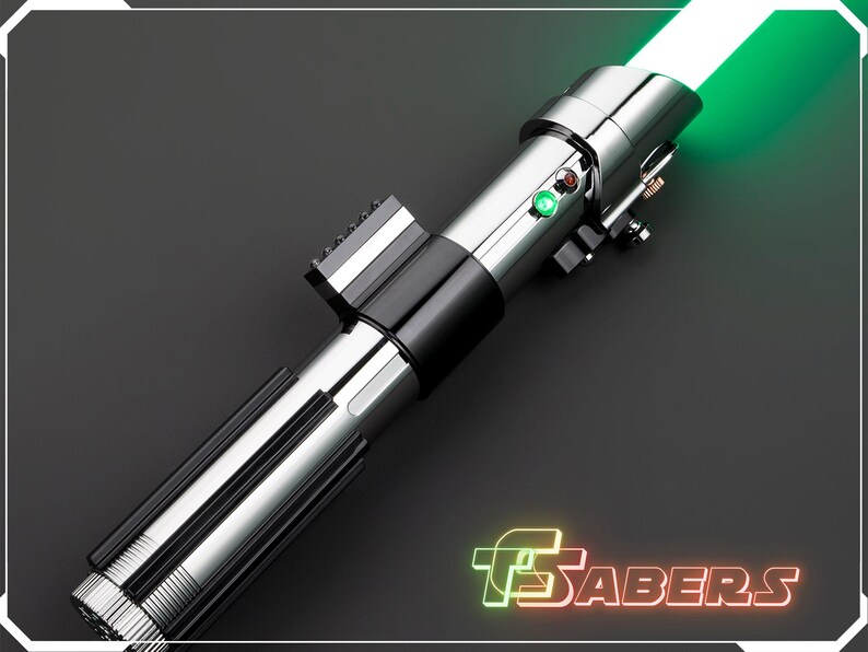 May include: A silver and black lightsaber with a bright green blade. The hilt features a ribbed design and several buttons and switches. The text "TSABERS" is displayed in neon green and red.