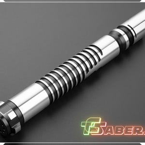 Puede incluir: Un sable de luz plateado y negro con un dise&ntilde;o de empu&ntilde;adura acanalada y un emisor biselado. El sable de luz tiene un pomo negro y una hoja plateada. El logotipo "TSabers" est&aacute; en la esquina inferior derecha.