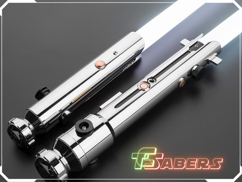 Puede incluir: Dos sables de luz cromados con hojas blancas se muestran sobre una superficie oscura. Cada sable tiene un mango cil&iacute;ndrico con detalles, incluyendo botones naranjas y negros. El logotipo "TSABERS" es visible en la esquina inferior derecha.