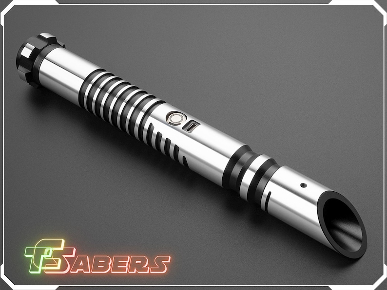 Puede incluir: Un sable de luz plateado y negro con un dise&ntilde;o cil&iacute;ndrico. El mango presenta anillos negros y un bot&oacute;n. La punta tiene una abertura negra. La imagen incluye el texto "TSABERS" en una fuente de estilo ne&oacute;n.