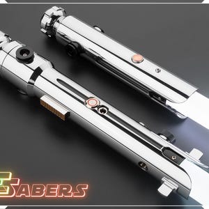 Puede incluir: Dos sables de luz cromados con hojas blancas se muestran en diagonal. Cada sable tiene un mango detallado con botones y una hoja brillante. La imagen incluye el texto "TSABERS" en una fuente de estilo ne&oacute;n.