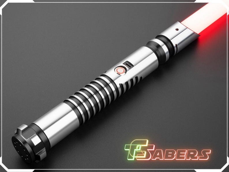 Puede incluir: Un sable de luz plateado y negro con una hoja roja. El mango presenta un dise&ntilde;o acanalado con detalles en negro y un bot&oacute;n de encendido. La imagen incluye el texto "TSABERS" en una fuente de estilo ne&oacute;n.