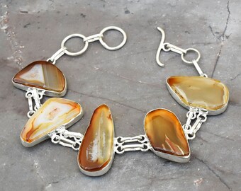 May include: A silver bracelet with a toggle clasp features five brown agate stones with white patterns. The stones are connected by silver links.