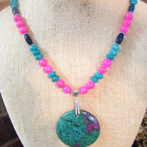 May include: A necklace with pink and teal beads and a large round green and pink gemstone pendant.