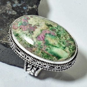 May include: A silver ring with an oval-shaped green and pink gemstone. The ring has a decorative silver band.