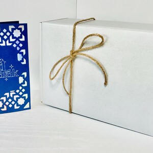 May include: A white gift box tied with twine and a blue card with a white geometric pattern and the text "Eid Mubarak".