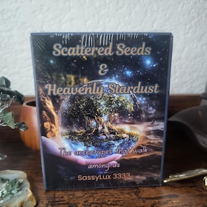 May include: A deck of cards with a blue background and a globe with a tree inside. The text on the front of the deck reads "Scattered Seeds & Heavenly Stardust The archetypes that walk among us SassyLux 3333".