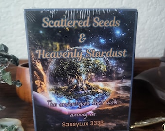 May include: A deck of cards with a blue background and a globe with a tree inside. The text on the front of the deck reads "Scattered Seeds & Heavenly Stardust The archetypes that walk among us SassyLux 3333".