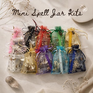 May include: A collection of ten small organza drawstring bags in various colors including pink, black, red, green, yellow, white, gold, purple, light blue, and dark blue, each printed with gold stars and moons and labeled Mini Spell Jar Kits.