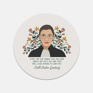 May include: A round, off-white coaster featuring an illustration of Ruth Bader Ginsburg, surrounded by floral elements in shades of pink, yellow, and green. The coaster includes a quote by Ginsburg and her name in a script font.