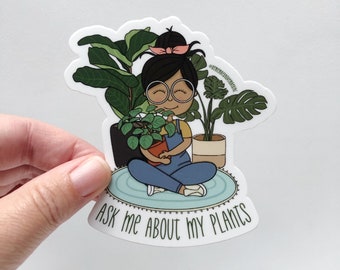 May include: A sticker featuring a cartoon illustration of a person surrounded by potted plants. The person is wearing glasses and overalls, sitting on a blue rug. The sticker reads "ASK ME ABOUT MY PLANTS."