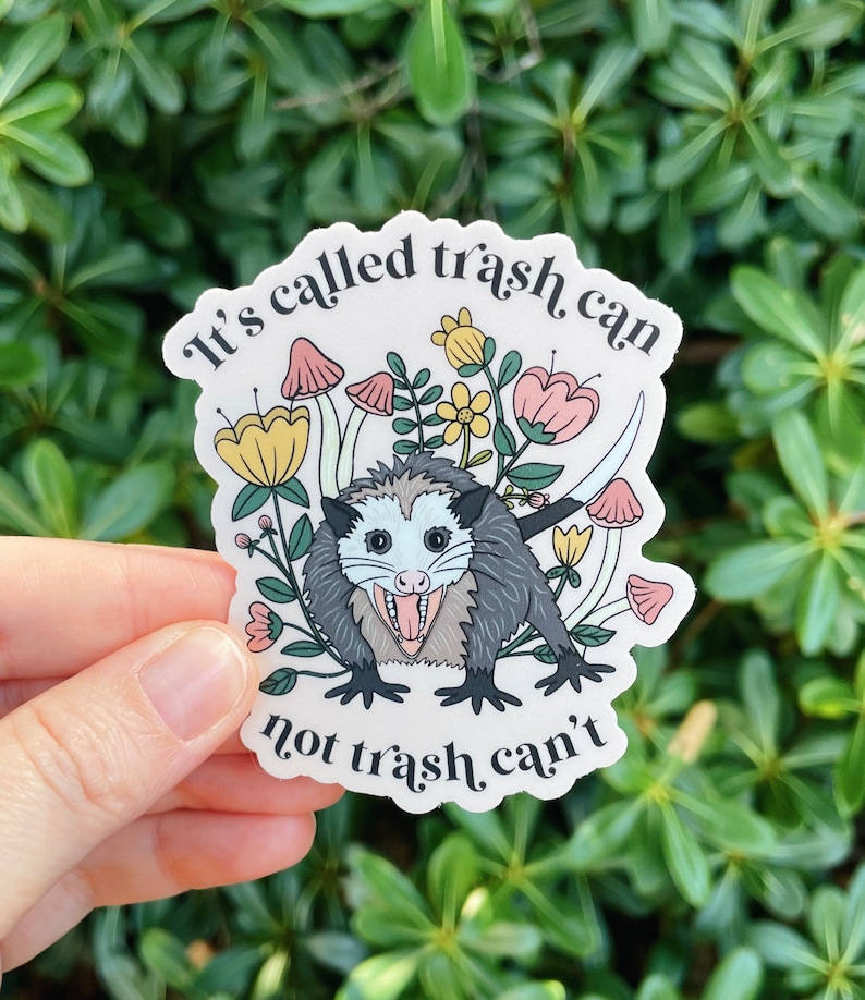 May include: A white sticker with a cartoon possum surrounded by flowers and mushrooms. The text on the sticker reads "It's called trash can not trash, can't".