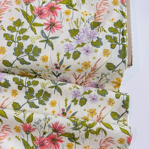 May include: A roll of floral fabric featuring a cream background with a repeating pattern of pink, yellow, and purple flowers, along with green leaves and stems. The fabric is folded and ready for use.