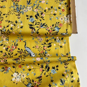 May include: Yellow fabric with a floral and bird print. The fabric features a repeating pattern of black branches with blue and white flowers, red berries, and small blue birds. There are also larger birds with long necks and tails.